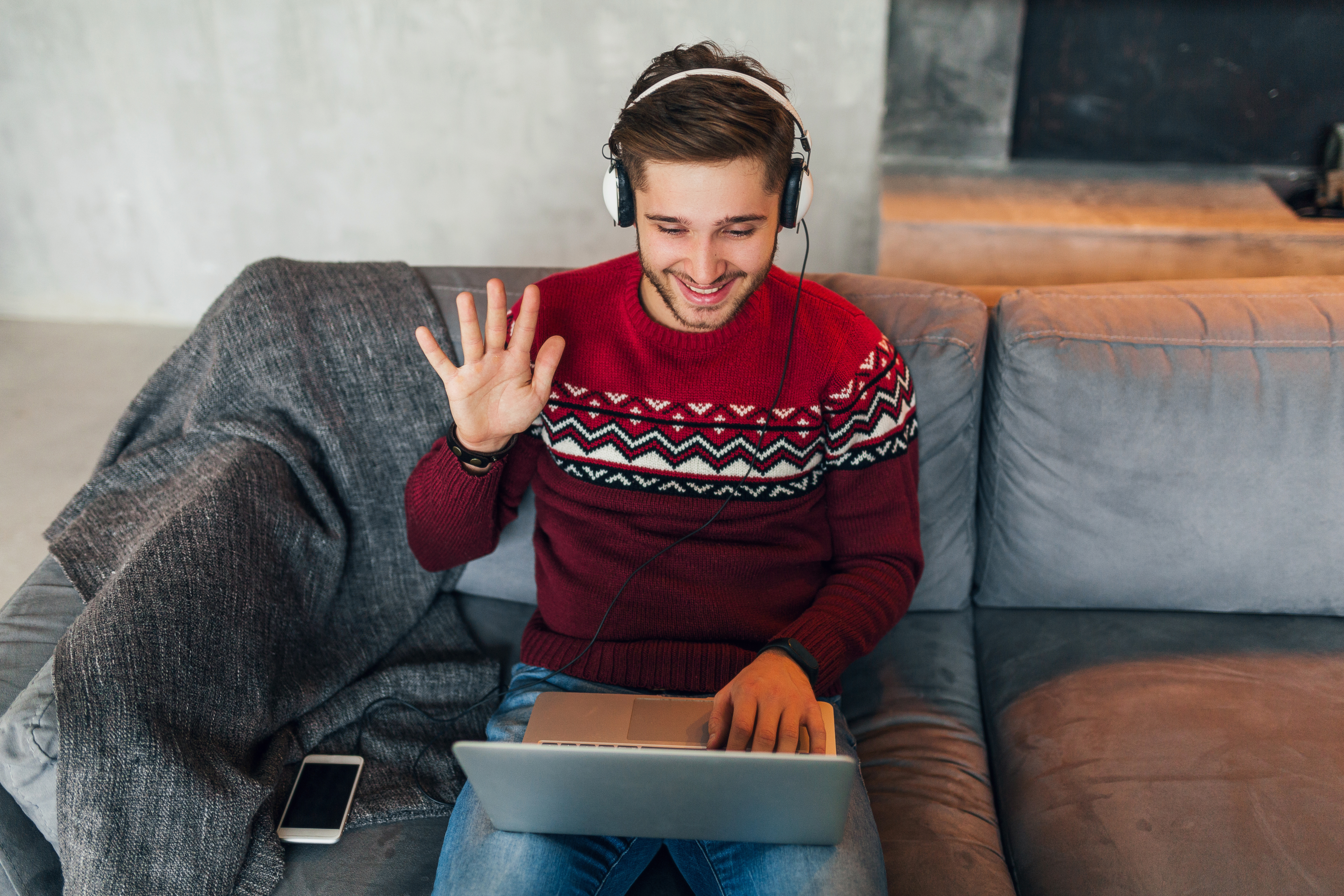 young-smiling-man-sitting-home-winter-having-conversation-online-waving-hand-saying-hello-wearing-red-sweater-working-laptop-freelancer-listening-headphones-studying-online.jpg